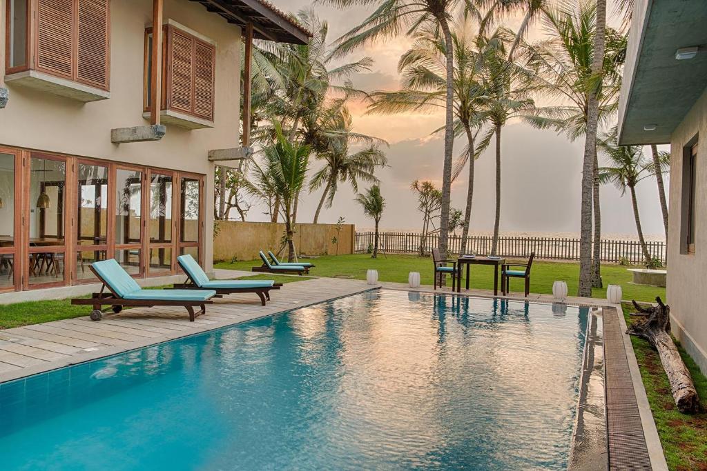 a swimming pool with blue chairs and palm trees at Villa 700 by Amaya in Bentota