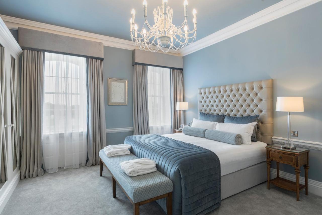 Elegant bedroom with a chandelier, tufted headboard, large bed, blue accents, and natural lighting.