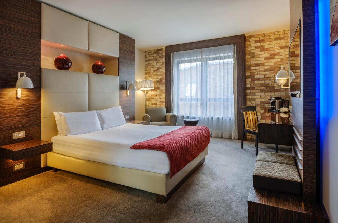 Modern hotel room with a large bed, brick accent wall, and ambient lighting.