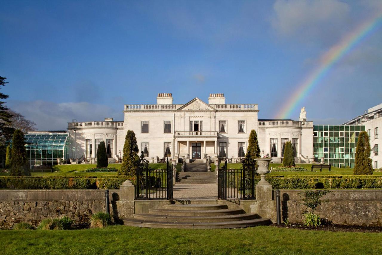 Grand estate with manicured gardens, wrought iron gates, and a rainbow in the background.