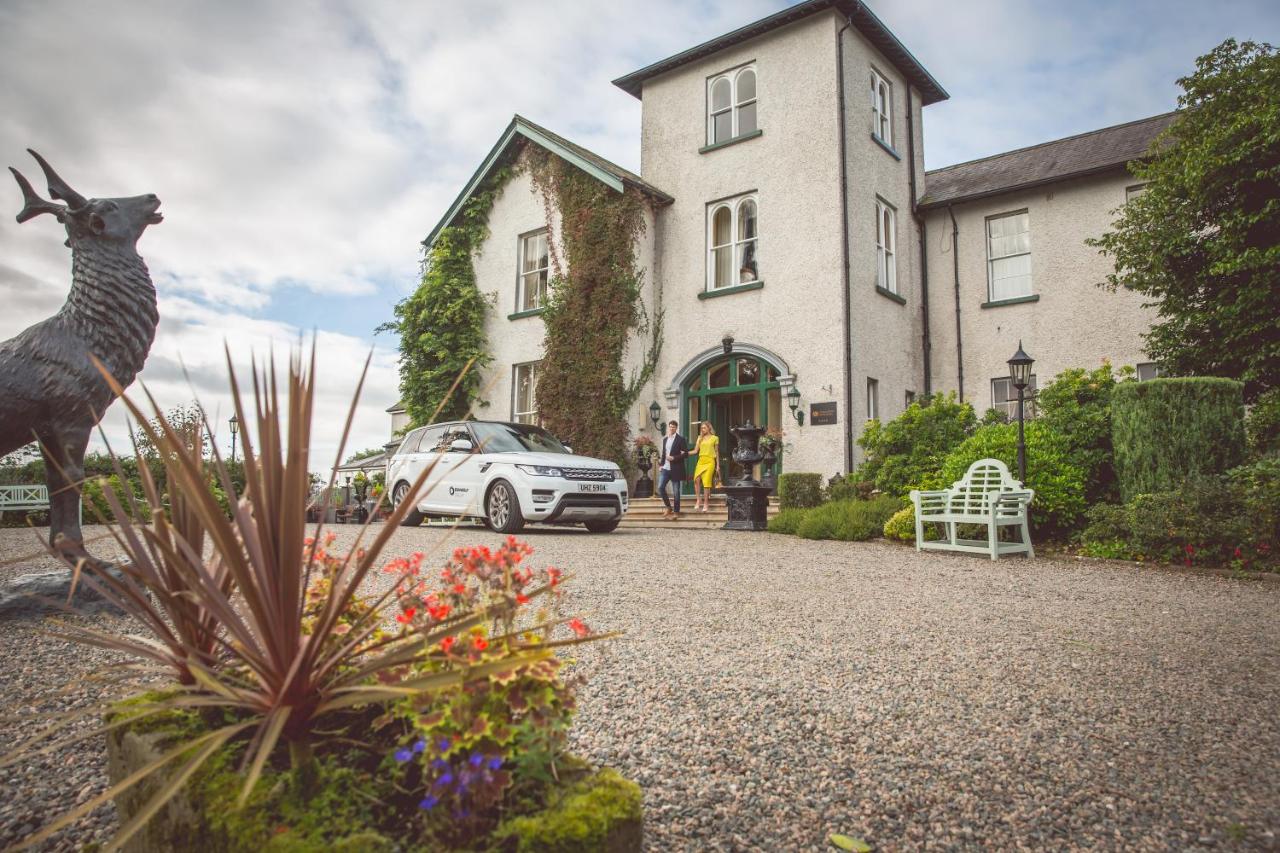 A large house with a white car in front, surrounded by greenery and flowers.