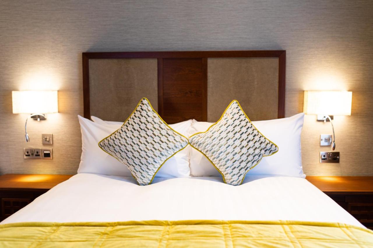 Well-made hotel bed with white linens and decorative pillows, flanked by two wall-mounted lamps.