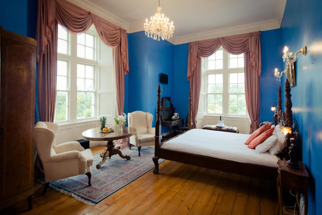 Luxurious bedroom with blue walls, large windows, vintage furniture, and a chandelier.