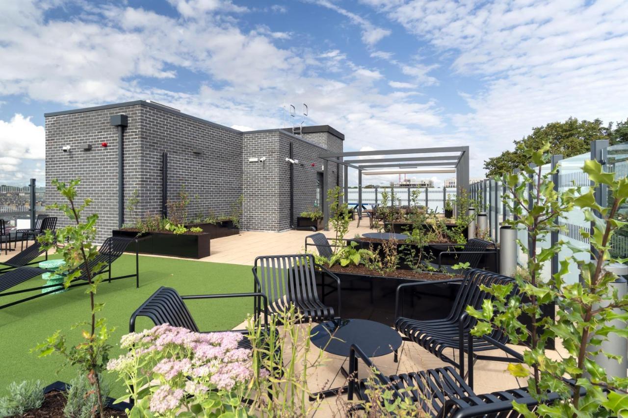 Rooftop garden with planters, seating, and pergola against a city skyline.