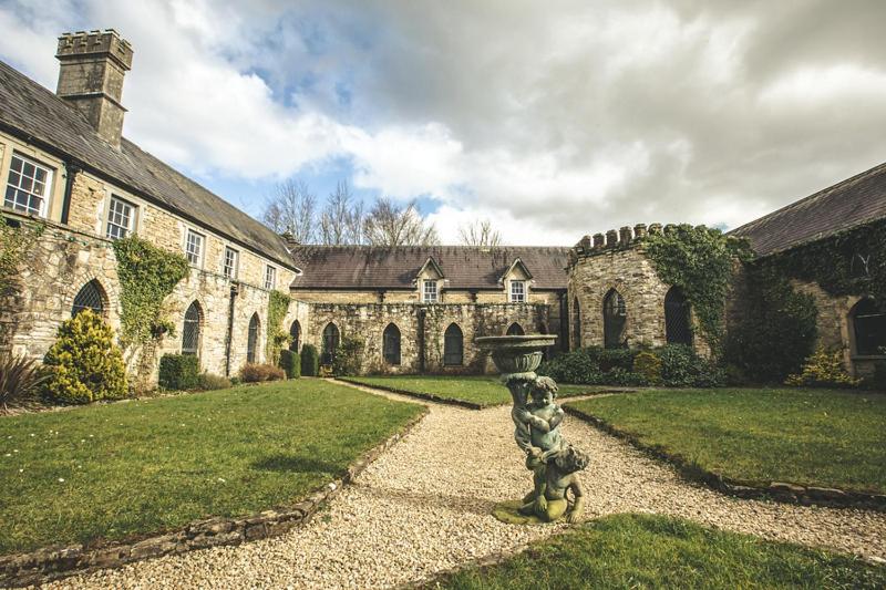 A historic stone courtyard with green lawns and a central cherub statue fountain.