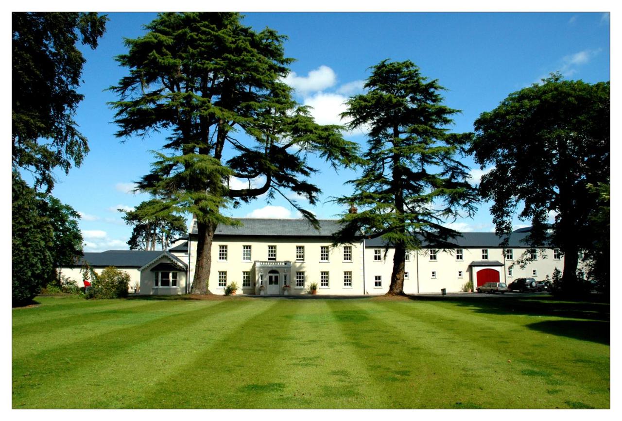 A large white building with tall trees and a spacious green lawn in front.